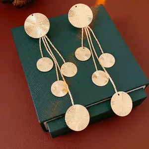Golden round textured drop earrings with long chain tassels on a jewelry display case