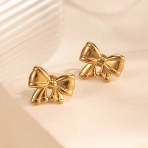Elegant gold bow-shaped stainless steel stud earrings on a textured stone surface