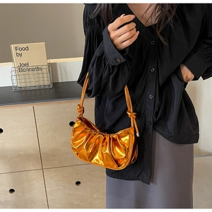 Detail of metallic orange pleated shoulder bag showing glossy texture and slim strap