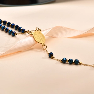 Macro detail of dark blue faceted beads and golden religious medal on a cross necklace
