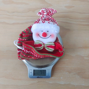 Detailed top view of a knitted snowman Christmas gift bag weighed on a kitchen scale