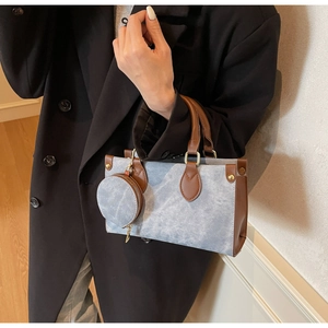 Detail of blue denim textured handbag with brown leather trim and round coin purse