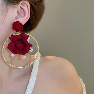 Detail view of large red fabric rose earrings with gold hoop and pearls on a female model