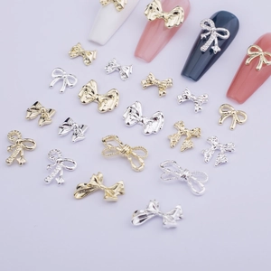 Detail of 3D metal bow nail art charms in gold and silver finish on a purple background