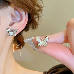 Detailed close-up of a silver butterfly stud earring with fine textured metal engraving