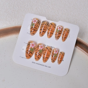 Macro detail of tiger print press-on nails with 3D pink flowers on a white plate
