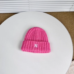 Detail of rose pink cuffed knit beanie showing white embroidered N letter and ribbed texture