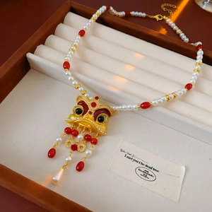Dettaglio della collana vintage con ciondolo leone dorato, nappe rosse e perle