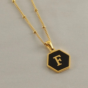 Detail of a golden hexagon pendant with a black center featuring the letter F