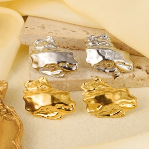 Abstract irregular earrings in gold and silver finish displayed on a beige stone block