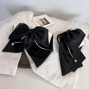 Detail of black bow hair clip with white piping and pearls on a wooden tray