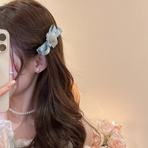 Detail of light blue satin bow hair clip with white fabric rose on model's hair