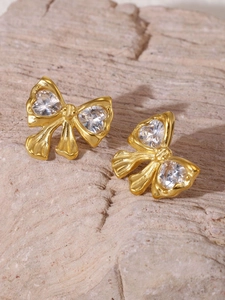 Macro view of gold bow earrings with heart-shaped zircon on textured stone surface