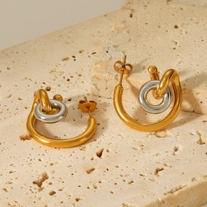 Two-tone gold and silver curved stainless steel hoop earrings on a stone background
