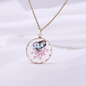 Macro view of a gold resin pendant featuring dried pink flowers and a colorful butterfly