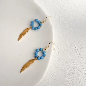 Detail of bohemian turquoise bead earrings with golden feather pendants on a white plate