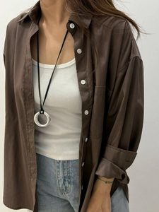 Detail of silver mirror ring pendant on black leather cord styled with brown shirt