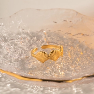 Macro detail of golden seashell-shaped stainless steel ring on a glass tray