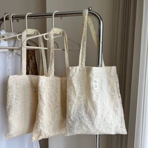 Detailed embroidery view of vintage lace tote bags in cream hanging on hangers