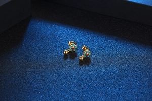 Detailed view of a gold floral earring with teal enamel petals and a hanging ball drop