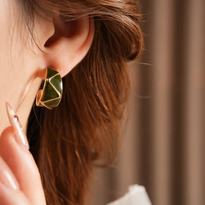 Detail view of a model wearing green enamel C-shaped earrings with gold geometric design