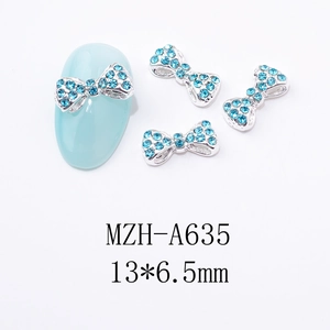 Détail de bijoux d'ongles nœud argenté avec strass bleus sur manucure bleu clair