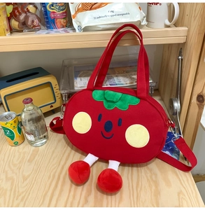 Detail view of red tomato canvas bag with 3D embroidery and plush limbs on wooden shelf