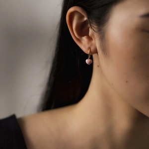 Close-up of a model wearing a gold hoop earring with a pink heart-shaped pendant