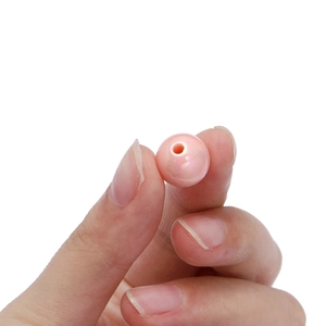 Nahaufnahme einer rosa Acrylperle mit Perlmuttglanz und Mittelloch in der Hand
