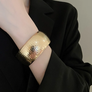 Detail of wide golden hammered texture cuff bracelet worn over a sleek black suit