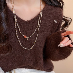 Detail of layered beaded necklace with reddish-brown pendant and star charm on a sweater