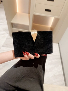 Elegant black velvet evening clutch bag with gold leaf-shaped clasp held by hand