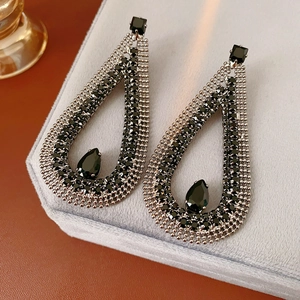 Detailed close-up of teardrop black zircon earrings on a grey velvet jewelry stand