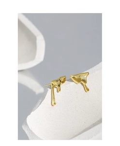 Macro detail of irregular gold molten lava earrings on white textured stone stand