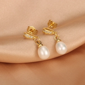Macro detail of 18K gold pearl earrings with zircon inlay on champagne satin fabric
