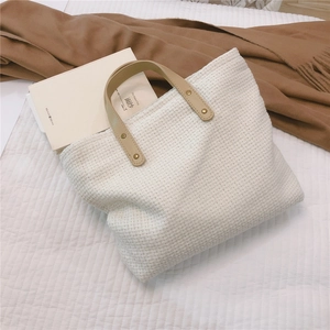 Detail of cream white tweed tote bag with brown PU leather handles on a cozy bed