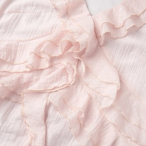 Close-up of light pink dress featuring layered ruffles and pleated vertical texture