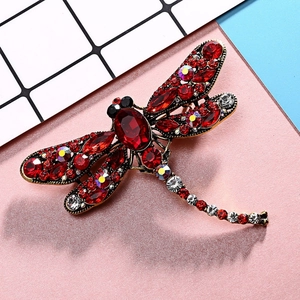 Detailed close-up of a vintage dragonfly brooch with red crystals and bronze finish