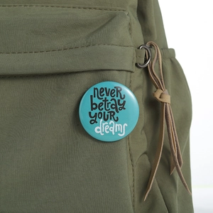 Never betray your dreams round pin badge on olive green canvas backpack accessory