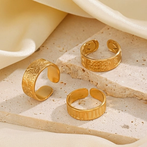 Three gold stainless steel adjustable open rings with embossed textures on travertine