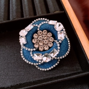 Detailed view of navy blue denim camellia brooch with rhinestones on black velvet display
