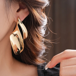 Macro detail of glossy gold abstract leaf-shaped statement earrings worn by a model