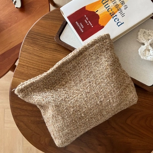Top view of a beige tweed makeup bag on a wooden table with a book and lace decor