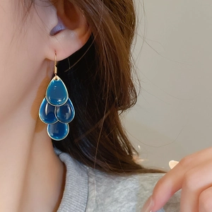 Macro view of blue teardrop tassel earrings with gold-toned hooks on a female model