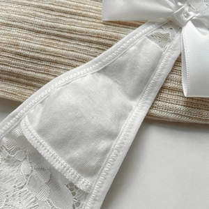Detailed view of white eyelash lace thong with satin bow and delicate floral patterns