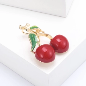 Fashionable cherry brooch featuring red enamel fruits and green leaves on gold branches