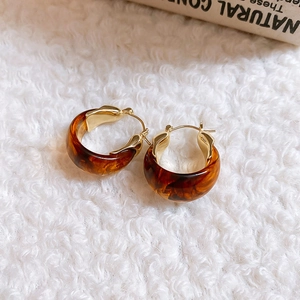 Close-up of amber tortoiseshell resin hoop earrings on a white soft plush background
