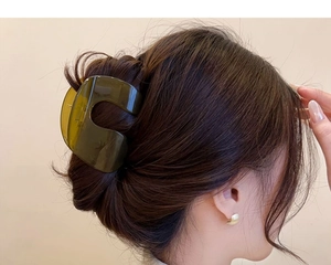 Detail of a large dark green transparent C-shaped hair claw clip on model hair