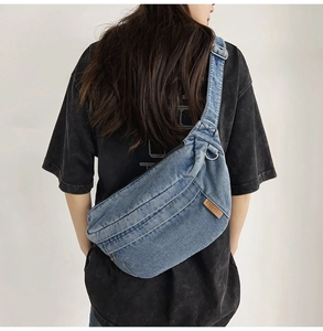 Rear view of a vintage blue denim crossbody bag featuring a wide strap and leather patch
