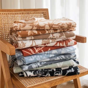 Folded elegant cashmere-like scarves with assorted prints stacked on a rustic wicker chair